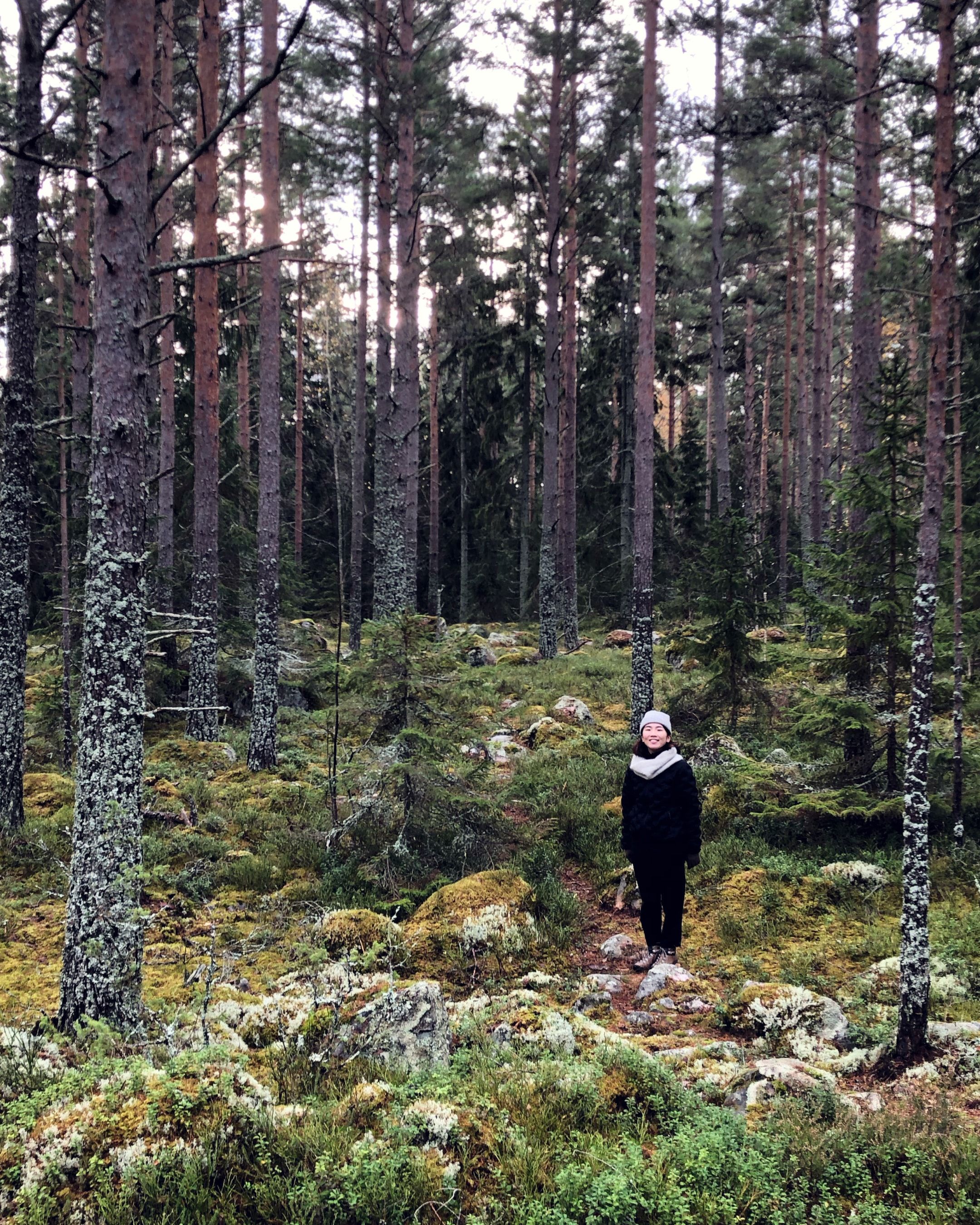 Yui Komatsu Lundqvist standing on a mossy path in a Swedish pine forest